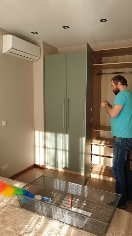 Мужчина сборщик мебели устанавотвает дверную ручку в шкафу Ikea: Муж на час в Риге